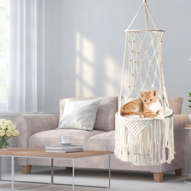 Ginger cat relaxing in a macrame cat swing bed, suspended in a stylish living room setting with neutral decor.