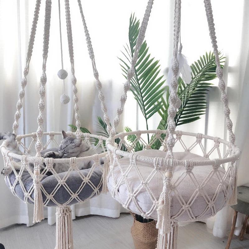 Two macrame cat swing beds hanging indoors with a cat resting inside, featuring a woven rope design and tassel details.